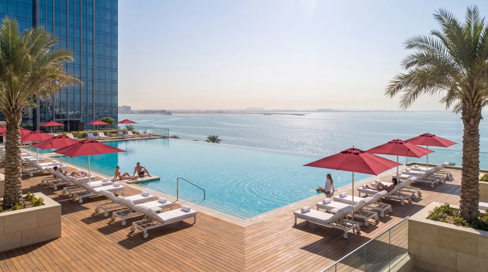 A rooftop infinity pool with red umbrellas at a seafront hotel.